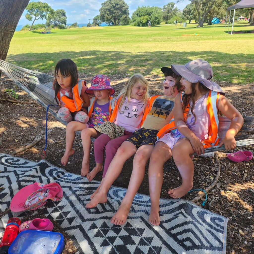 Children ages 5 to 12  laughing on a hammock, outside in the sunshine.